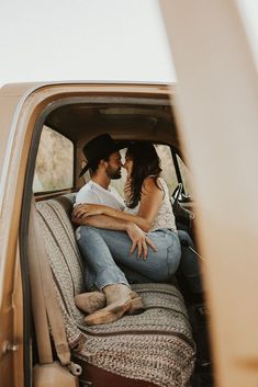 a man and woman sitting in the back of a pickup truck kissing each other while holding hands