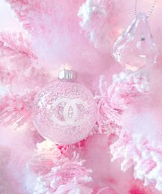 a chanel ornament hanging from a pink christmas tree with snow flakes