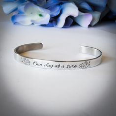 "Metal Stamped Cuff Bracelet that says \" One day at a time\" This is simple, elegant, and will look fantastic on your wrist. It also looks great stacked with other bracelets on your wrist as well. Every single detail of the design is hand stamped, and hammered in one by one, so slight variations in the stamping can be expected. You can order this bracelet with a hammered texture, mirror polish, or a satin finish. Mirror polish will show scratches and scuffs a bit more easily, but I include a po Texture Mirror, Stamped Metal, Small Bracelets, Inspirational Bracelets, Single Letter, Metal Bracelet, One Day At A Time, Copper And Brass, Stamped Jewelry