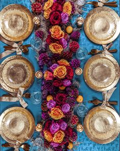 the table is set with gold plates and colorful flowers