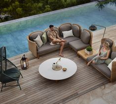 a man and woman sitting on couches next to a swimming pool in an outdoor setting