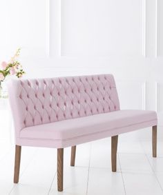 a pink bench sitting next to a vase with flowers in it on a white floor