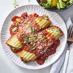 two white plates topped with lasagna shells next to a bowl of salad and fork