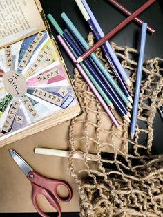 several colored pencils are laying next to an open book and some crochet hooks