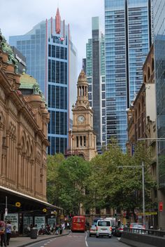 a city street with tall buildings in the background and a red bus driving down it