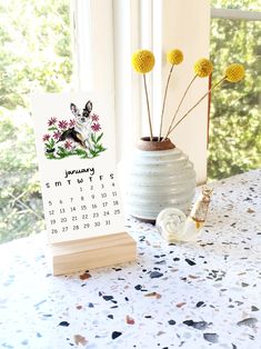 a table with a calendar and flowers in a vase next to the window on it