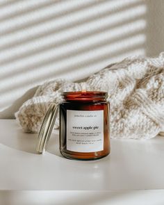 a candle sitting on top of a table next to a white blanket and a glass jar