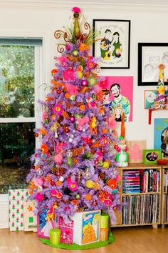 a brightly colored christmas tree in the corner of a room with pictures on the wall