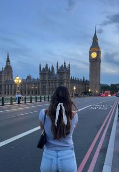 a woman standing in front of big ben and the houses of parliament at dusk, london