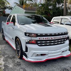 a white chevrolet truck parked next to other cars in a parking lot with palm trees