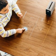 a young boy sitting at a table playing with an interactive board game on it's surface