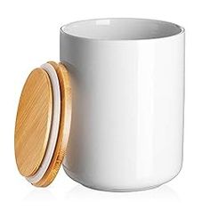 a white coffee cup with a wooden lid next to a container for tea or other drinks