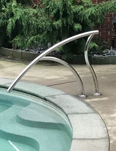 a cat sitting on the edge of a swimming pool next to a metal pole with an upside down design