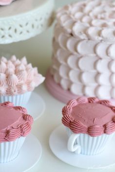 three cupcakes with pink frosting sitting on white plates next to each other