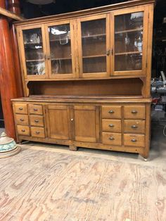 an old wooden china cabinet with glass doors on the front and bottom drawers, in a warehouse