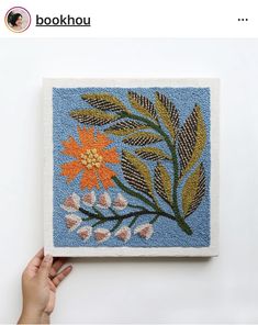 a hand is holding up a needle - embroidered square with flowers and leaves on it