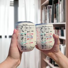 two people holding up coffee mugs in front of a book shelf filled with books