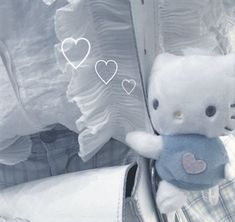 a hello kitty stuffed animal sitting on top of a pile of white shirts with hearts drawn on them