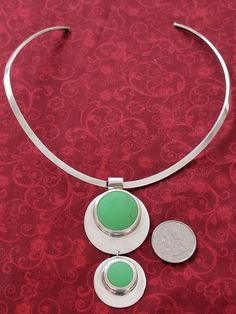 Sterling silver choker collar necklace with a large pendant.  The pendant consists of two silver discs with the smaller one hanging from the larger one.  Each silver disc has a large green stone that is off center.  It is a heavy piece of jewelry.  It is a beautiful, unusual necklace. Green Coin Pendant Medallion Jewelry, Green Necklace With Coin Pendant, Modern Green Round Pendant Jewelry, Modern Green Circular Jewelry, Green Coin Pendant Jewelry, Modern Green Necklace With Round Pendant, Green Medallion Pendant Jewelry, Green Medallion Jewelry With Large Pendant, Green Medallion Sterling Silver Jewelry