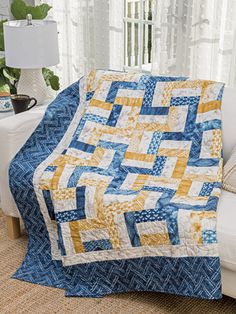 a blue and yellow quilt sitting on top of a white couch next to a window