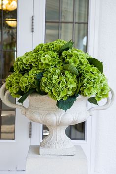 a white vase filled with green flowers sitting on top of a cement pedestal next to a door