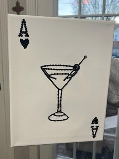 a white canvas with a black and white drawing of a martini glass on it, in front of a window