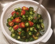 a white strainer filled with green and red peppers