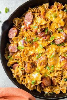 a skillet filled with pasta, sausages and cheese on top of a table