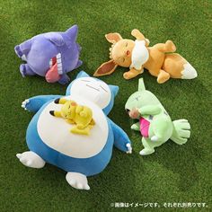 four stuffed animals laying on the grass in different colors and sizes, one with its mouth open