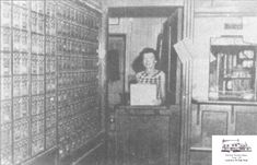 an old black and white photo of a woman standing in front of many mail boxes