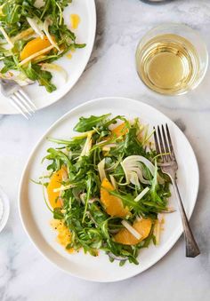 two white plates topped with salad on top of a marble table next to silverware