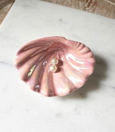 a pink shell with pearls on it sitting on top of a white marble countertop