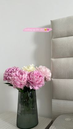 a vase filled with pink and white flowers on top of a table next to a bed