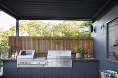 an outdoor kitchen with grill, sink and television on the counter top in front of a wooden fence