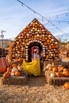 a woman standing in front of a fake house made out of hay and pumpkins