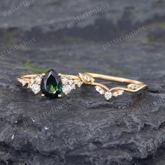 a green and white diamond ring sitting on top of a black rock with leaves around it