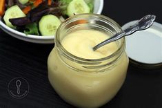 a salad in a jar with a spoon next to it and a bowl of dressing