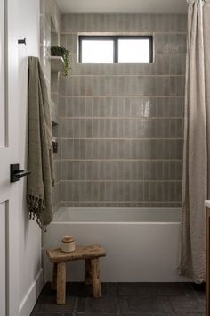 a white bath tub sitting under a window next to a wooden bench in a bathroom