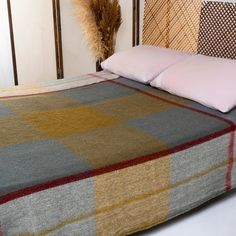 a bed with a checkered blanket and pillows on it, next to a plant