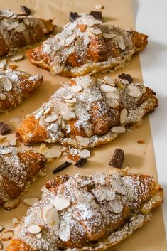 almond croissants with chocolate chips and powdered sugar on top, lined up on parchment paper