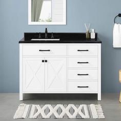 a white bathroom vanity with black counter top and mirror above it, along with a rug on the floor