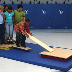 a group of children standing around a wooden bat on top of a blue mat in front of a wall