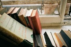 a pile of books sitting on top of a floor next to a window sill