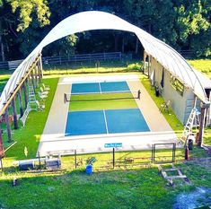 an aerial view of a tennis court surrounded by green grass and trees with chairs around it