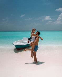 a man carrying a woman on his back while standing in the sand near a boat