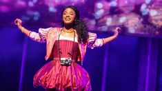 a woman in a pink dress is on stage with her arms out and hands outstretched