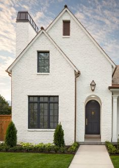 a white brick house with black shutters on the front door and windows, along with a walkway leading up to it