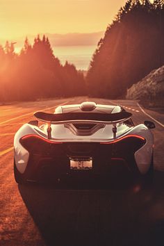 a white and red sports car driving down a road near the ocean at sunset or sunrise