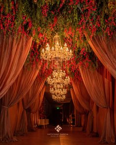 a chandelier hanging from the ceiling with red flowers and greenery on it