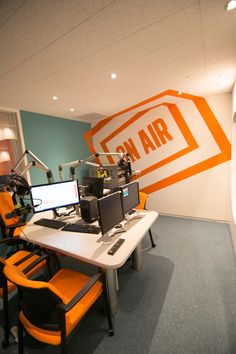 an office with two computers and orange chairs in front of a wall that says air